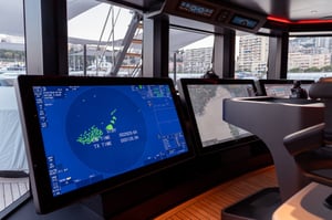 The image shows three floor-mounted 55-inch monitors on the bridge of superyacht Baglietto T52, docked at the Monaco Yacht Show 2023. They are part of Furuno's integrated bridge system for the yacht market. In the background you can see the bay of Monaco.